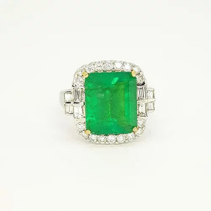 Emerald Cut Emerald and Diamond Cluster Ring; featuring a 4.18 carat emerald-cut emerald within a diamond surround, baguette cut diamond set shoulders, in 18ct white gold with heart detailing to the under-mount