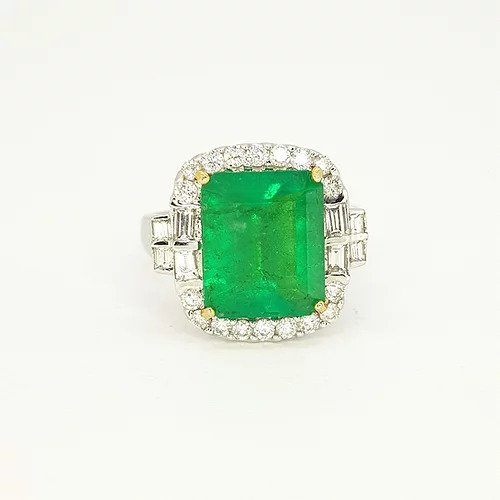 Emerald Cut Emerald and Diamond Cluster Ring; featuring a 4.18 carat emerald-cut emerald within a diamond surround, baguette cut diamond set shoulders, in 18ct white gold with heart detailing to the under-mount