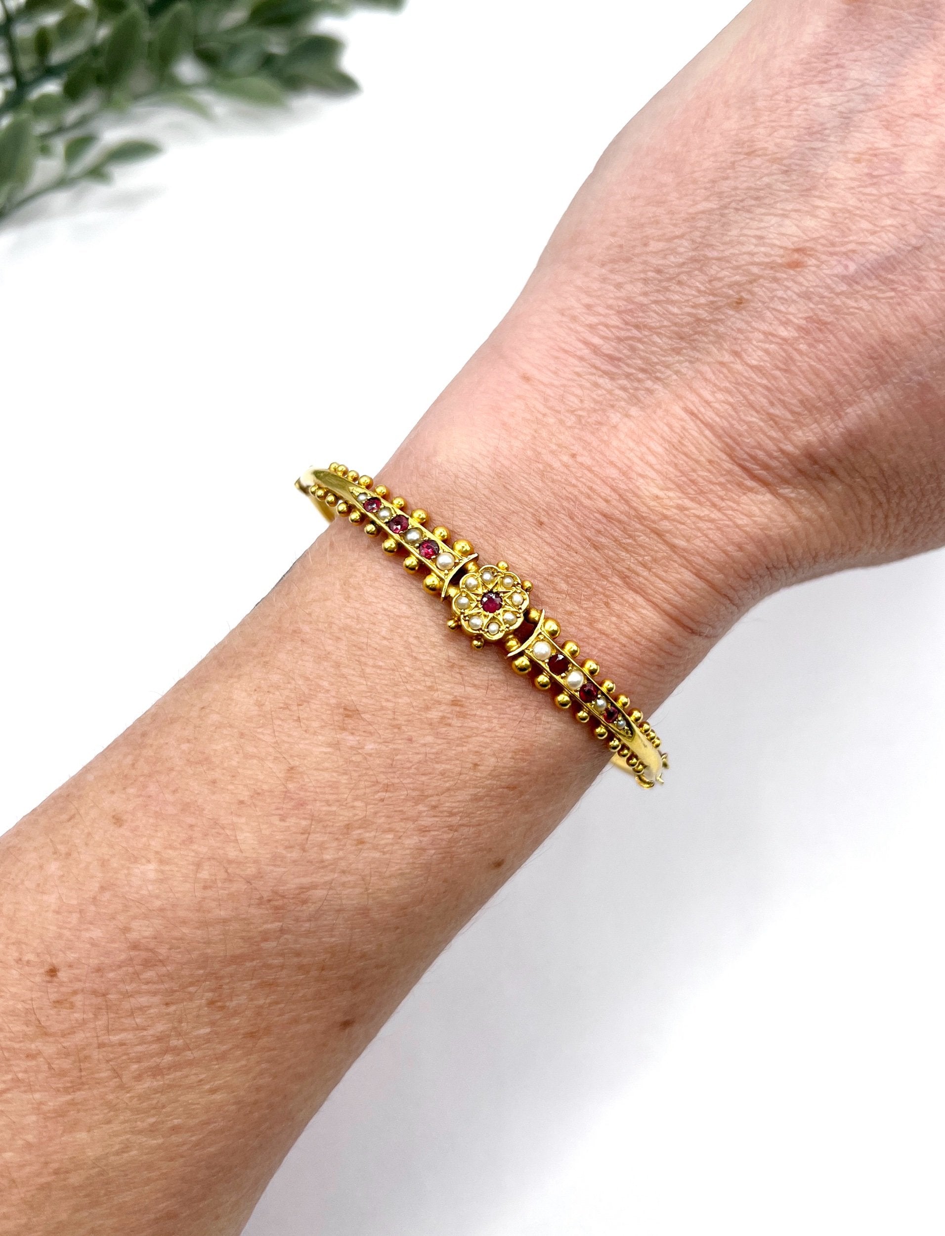 A yellow gold bangle bracelet set with rubies and seed pearls, modelled on a wrist
