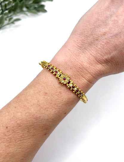 A yellow gold bangle bracelet set with rubies and seed pearls, modelled on a wrist