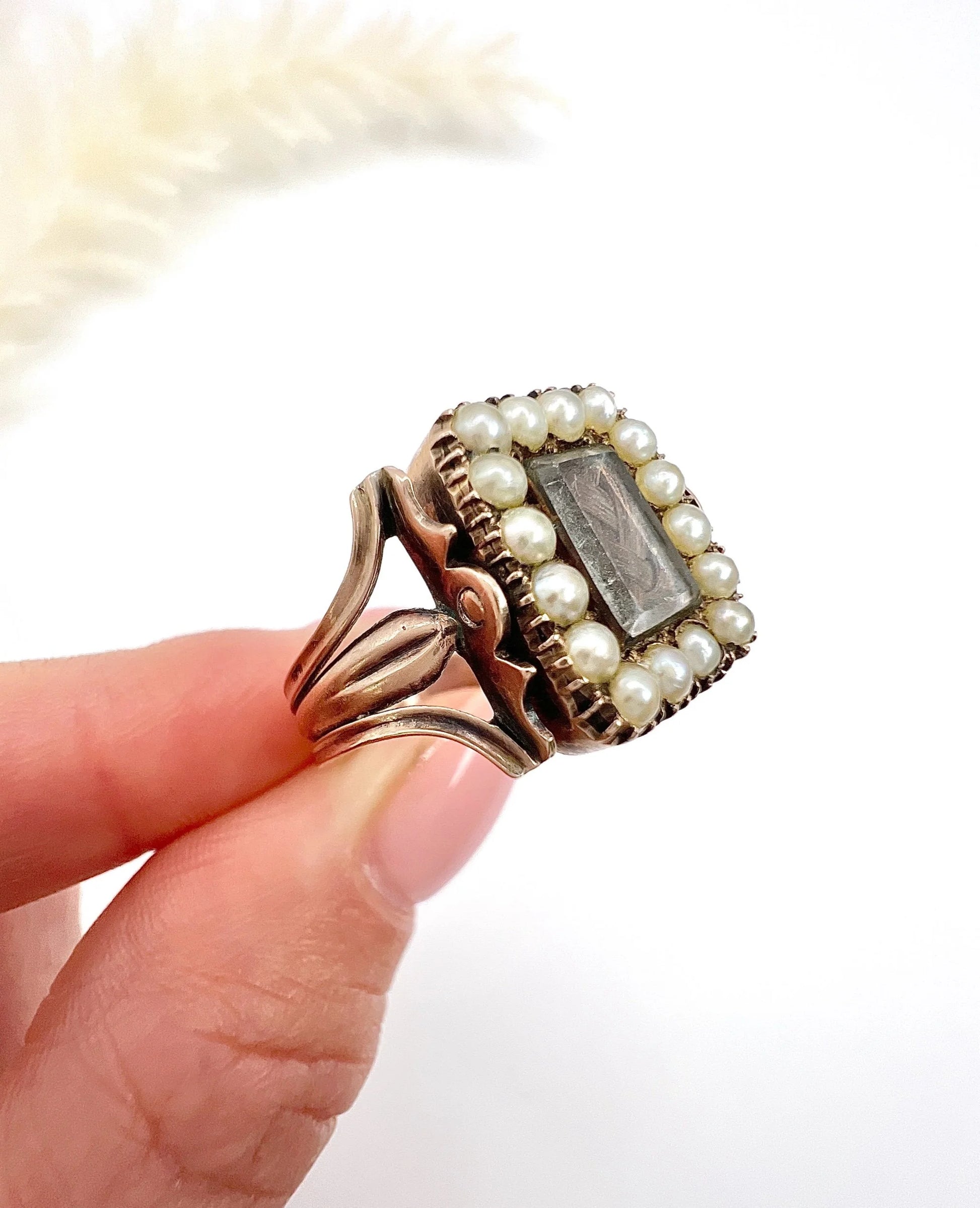 An antique seed pearl mourning ring in gold, held in a hand