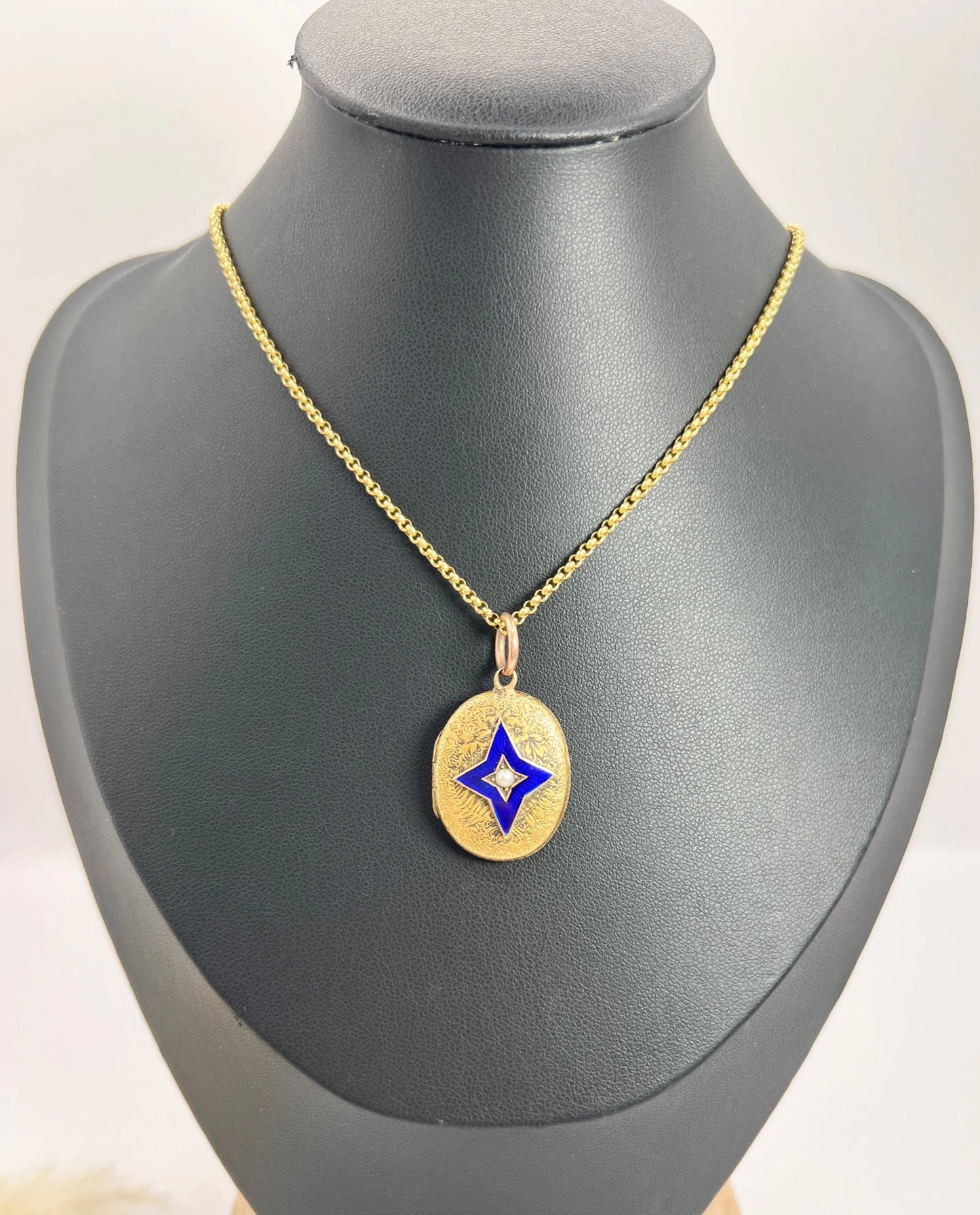 An oval yellow gold locket with a blue enamel star and seed pearl centr, with a chain