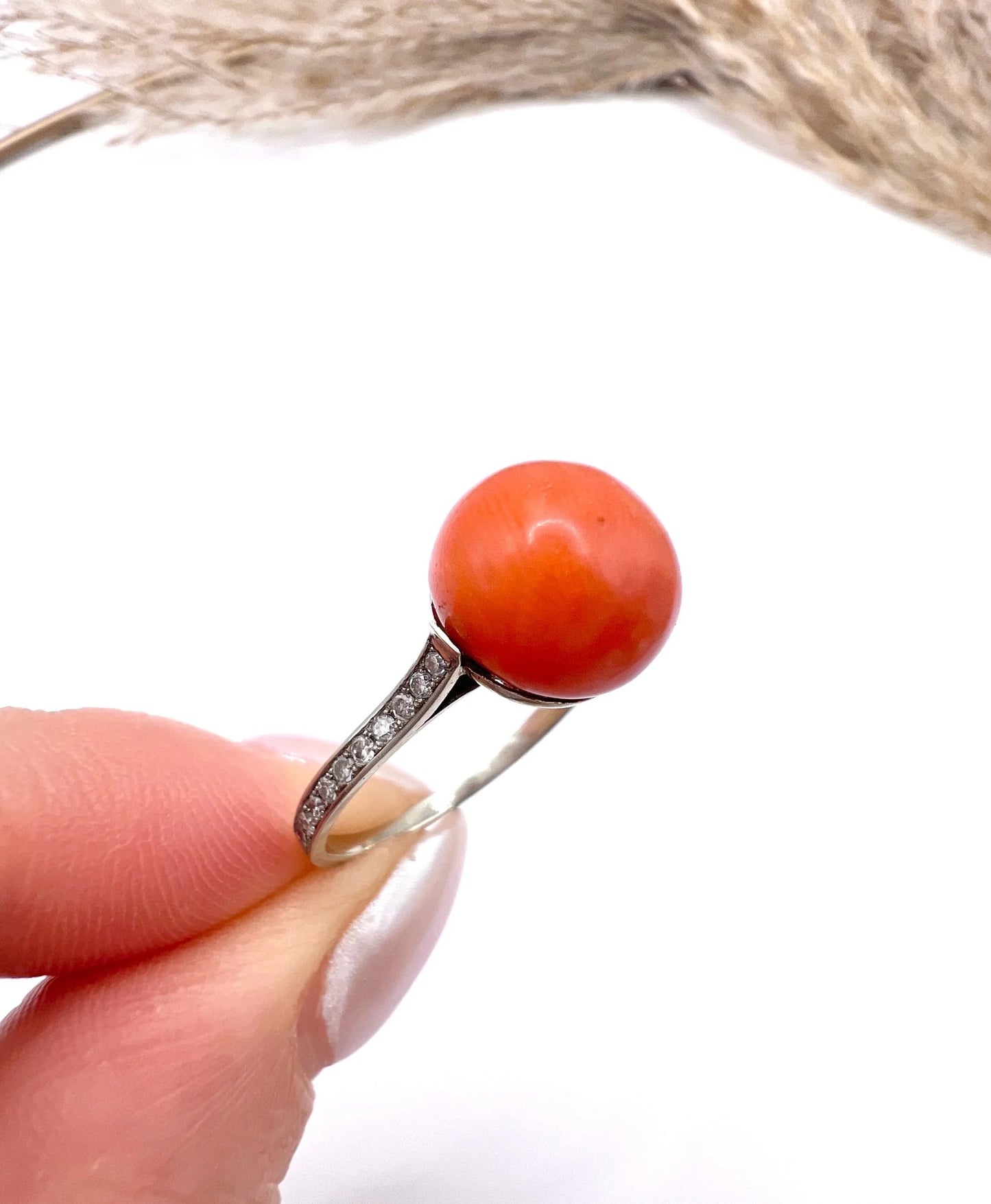 A round orange coral and diamond dress ring in platinum, held in a hand