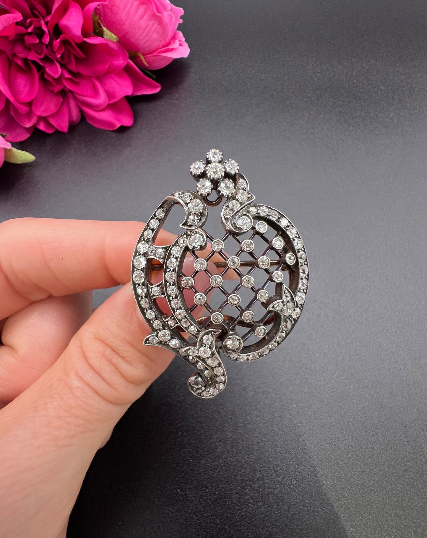 An openwork diamond set antique brooch in yellow gold and silver, held in a hand