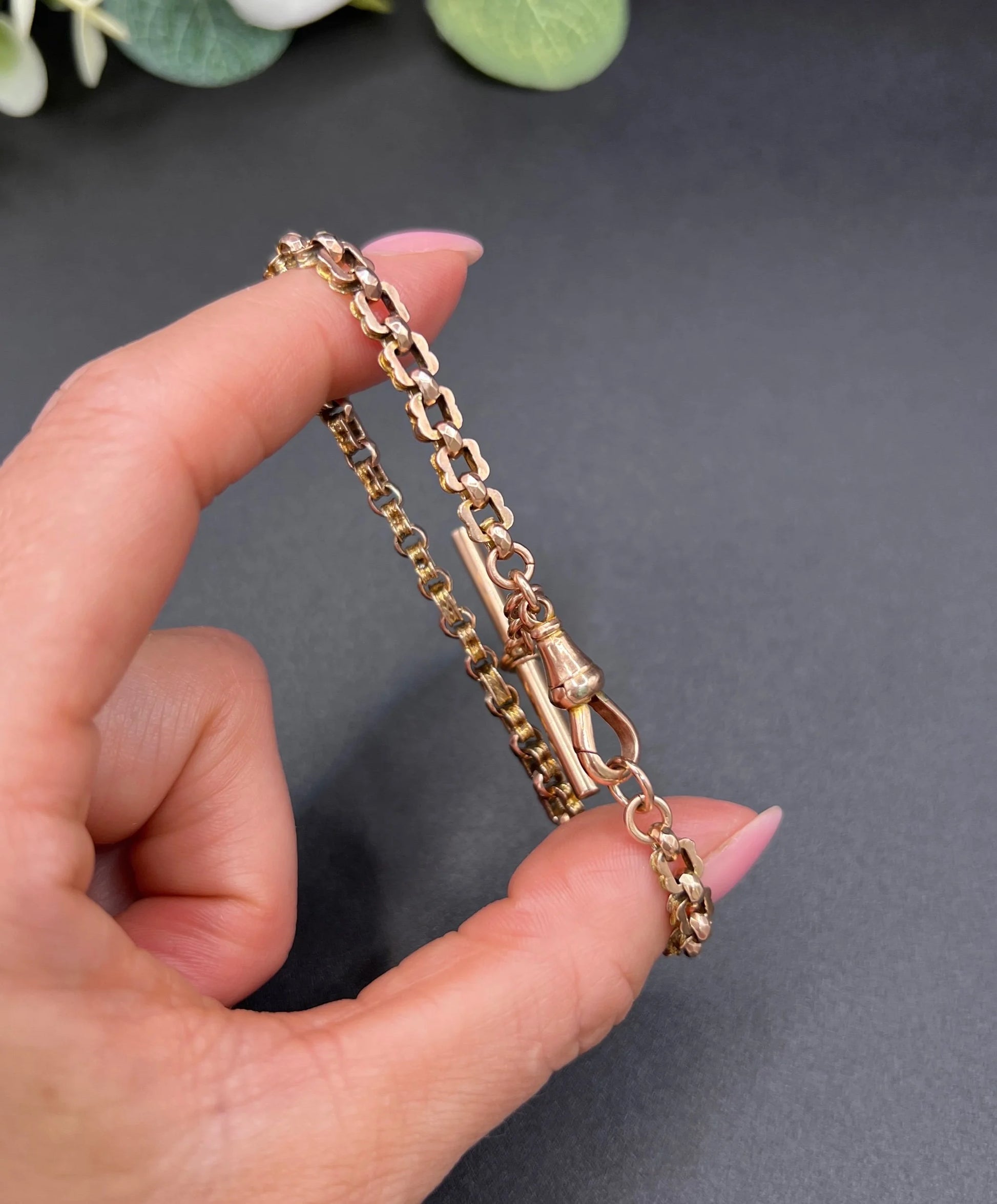 A fancy link rose gold bracelet with a T-bar and dog clip clasp, held in a hand