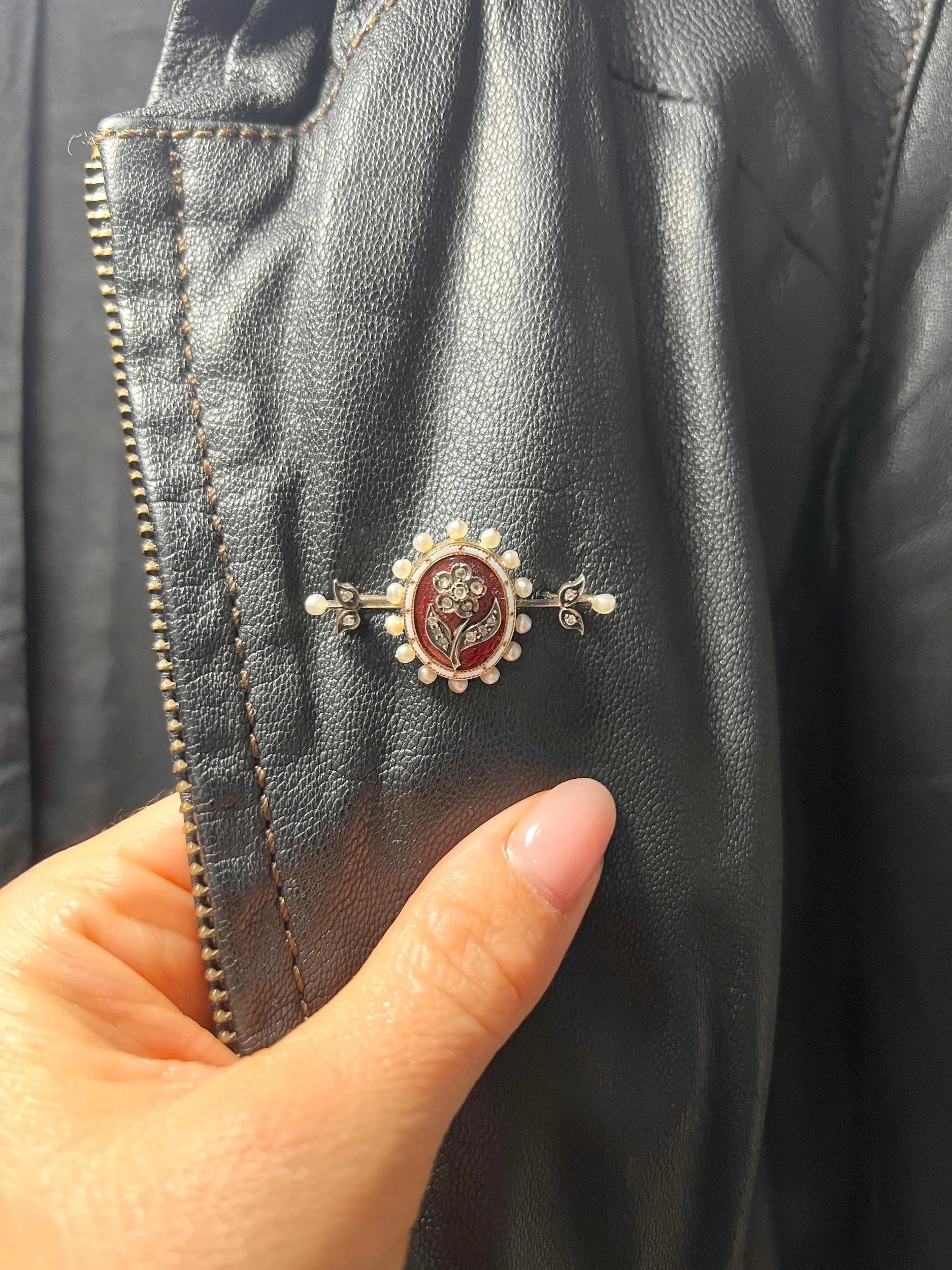 A yellow gold bar brooch with a red enamel centre surrounded by pearls, with a diamond flower motif and diamond leaves at either end, modelled on a jacket