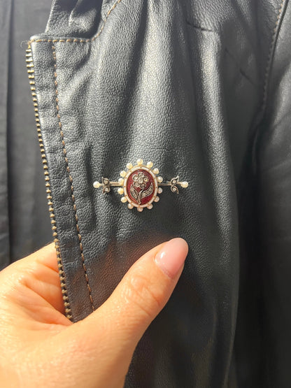 A yellow gold bar brooch with a red enamel centre surrounded by pearls, with a diamond flower motif and diamond leaves at either end, modelled on a jacket