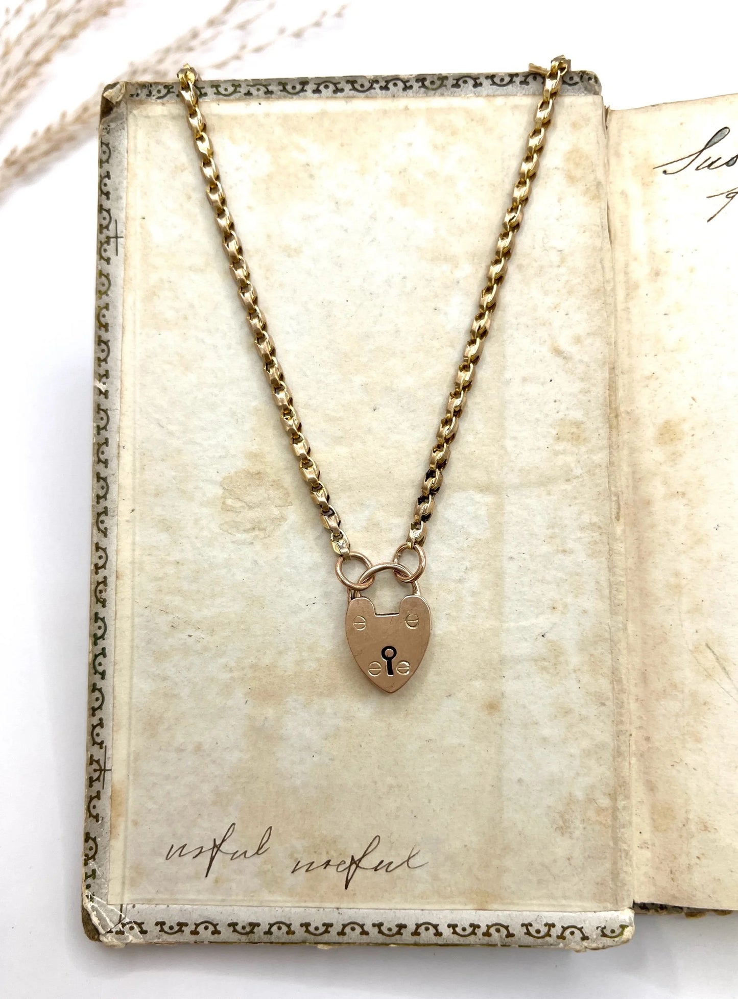 A gold chain necklace withgold heart padlock, on an antique book