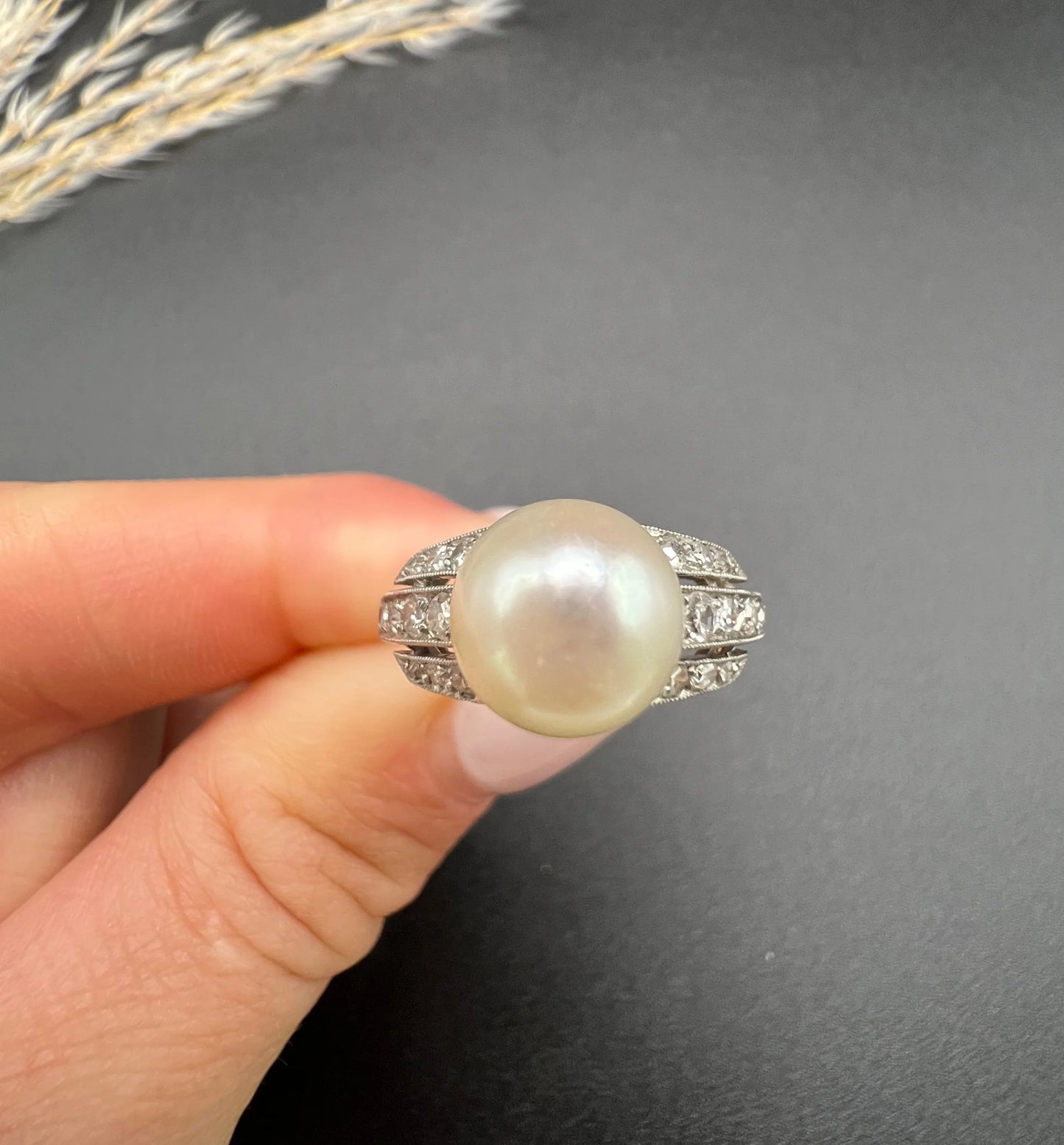 A pearl and diamond ring in platinum, held in a hand