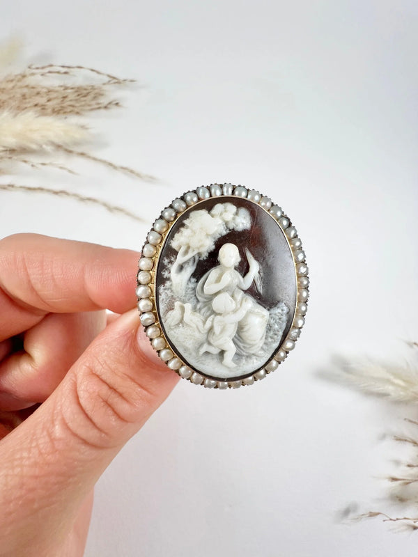 An antique oval cameo brooch depicting cherubs and birds, with a pearl border, set in gold