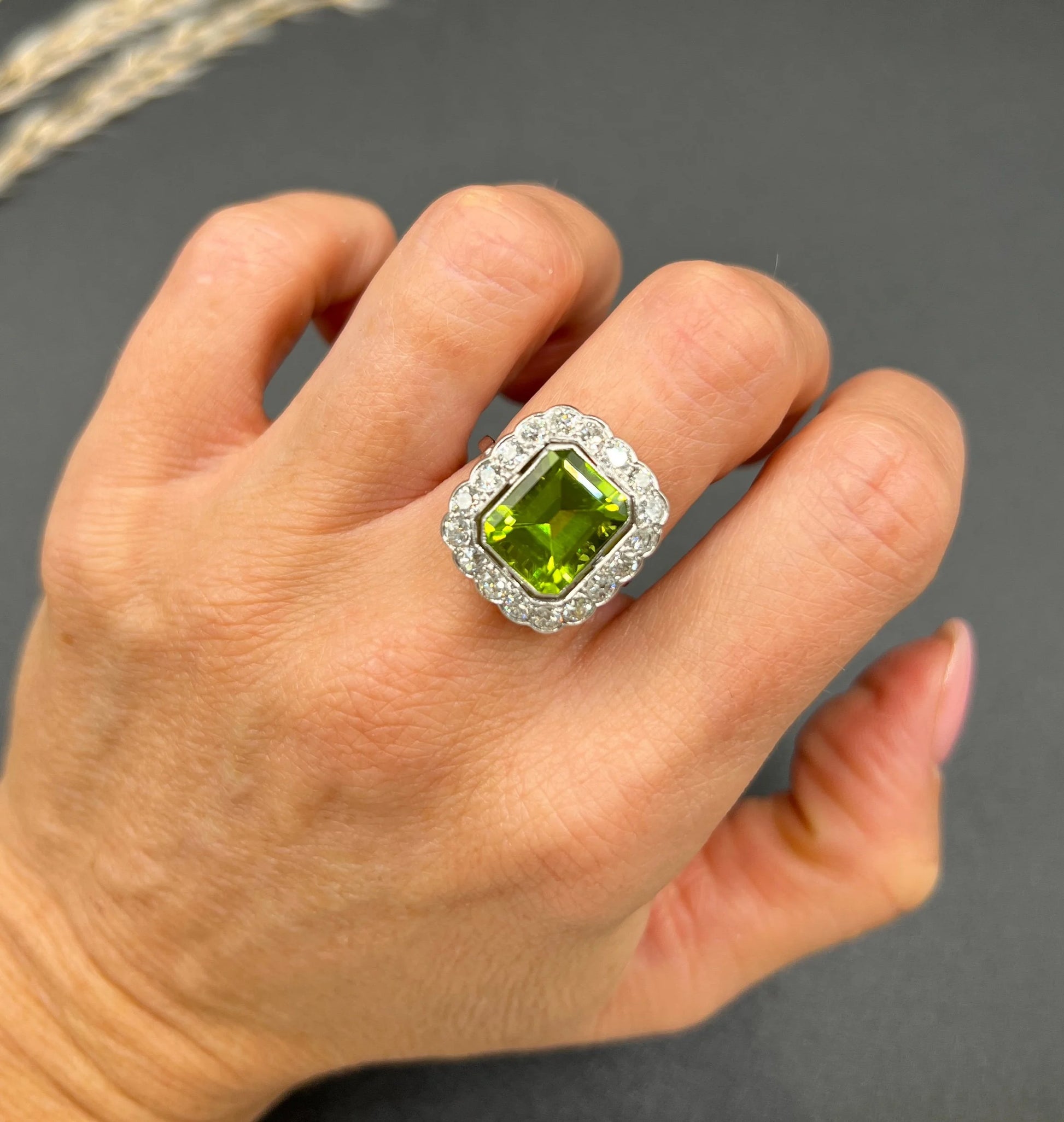 A cushion shaped peridot and diamond cluster ring in white metal, modelled on a hand