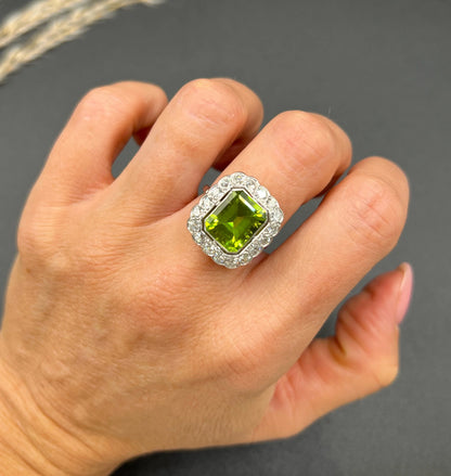A cushion shaped peridot and diamond cluster ring in white metal, modelled on a hand