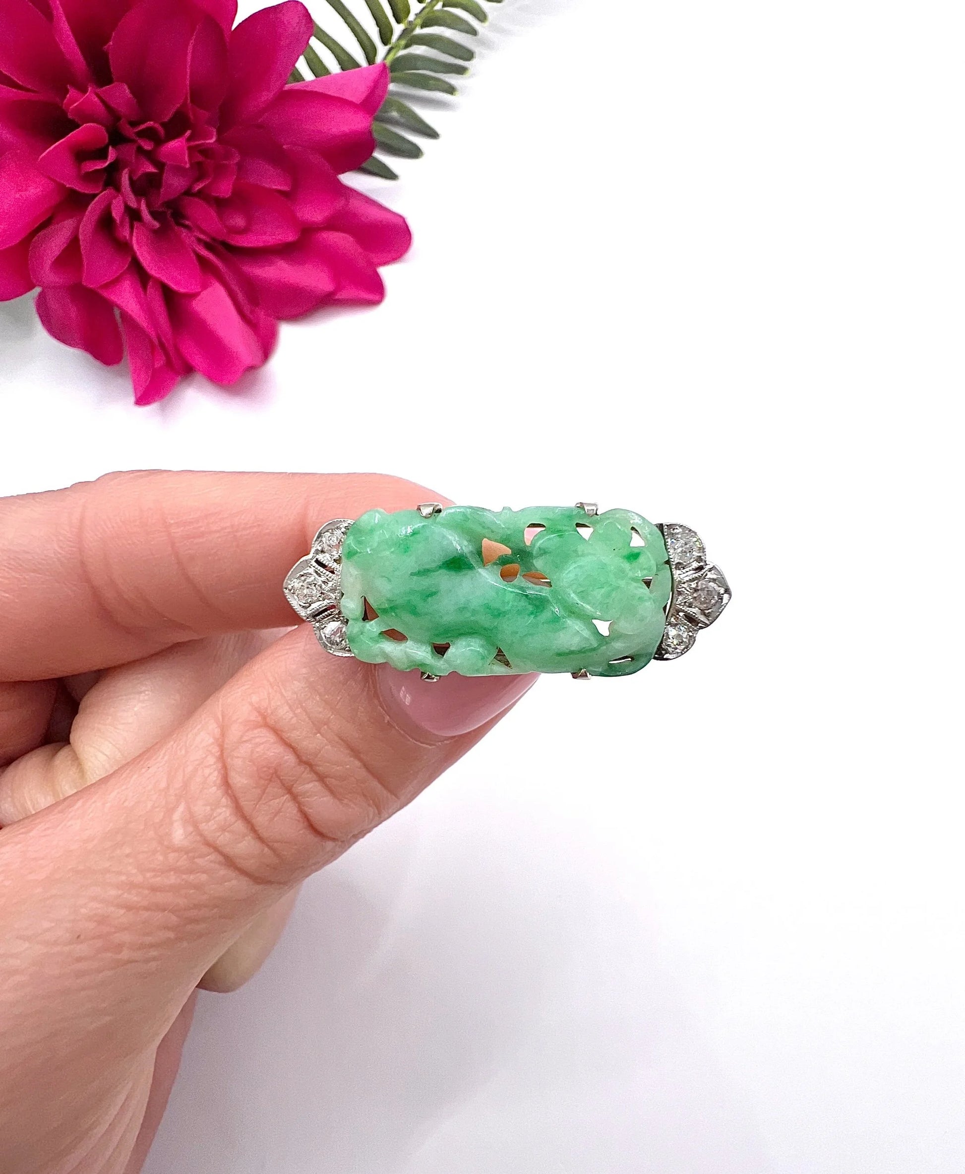 A carved green jade and diamond brooch in white gold, held in a hand