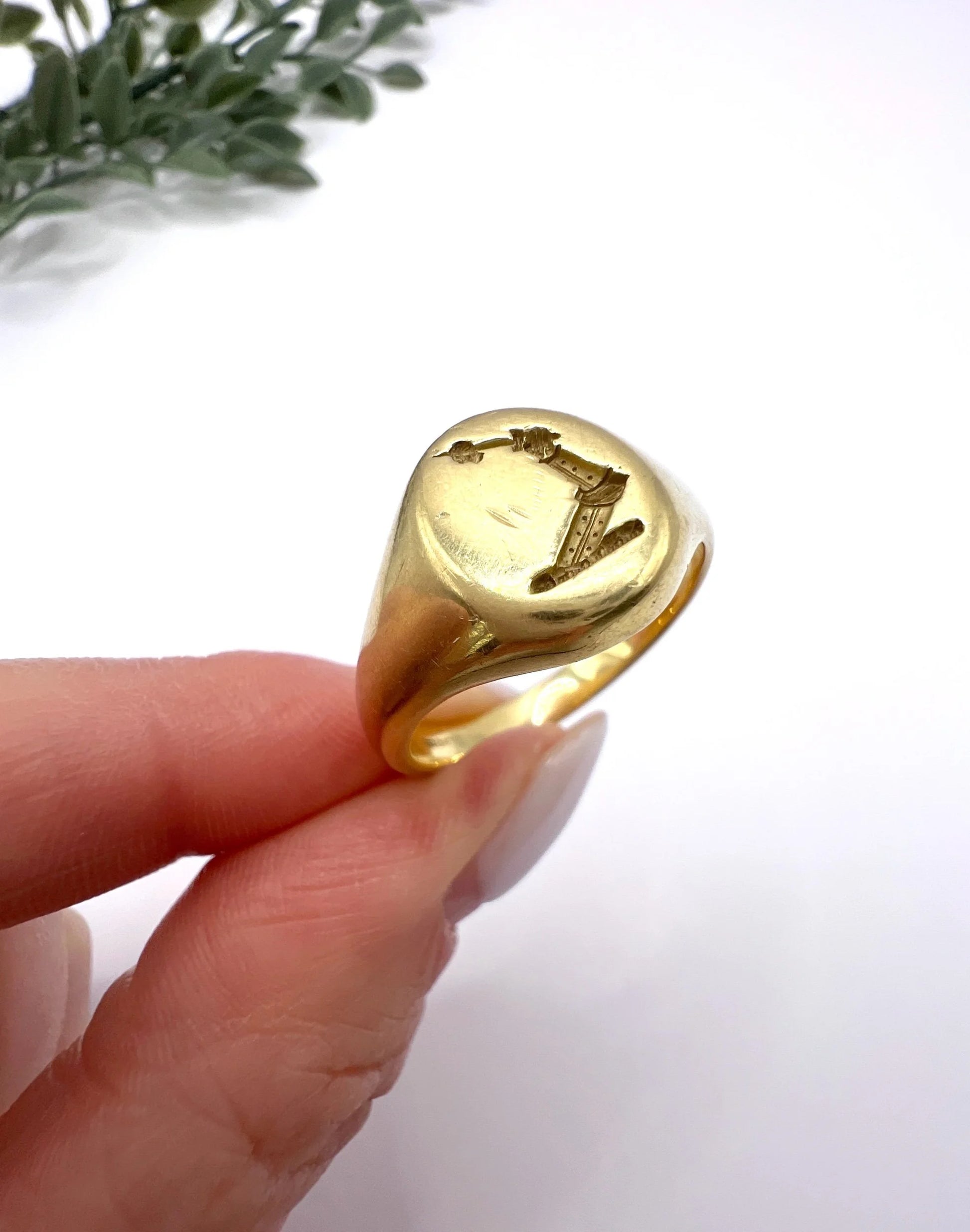 A yellow gold oval signet ring with a seal engraved heraldic crest, held in a hand