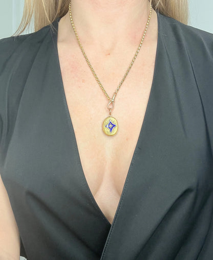 An oval yellow gold locket with a blue enamel star and seed pearl centre, with a chain, modelled by a woman