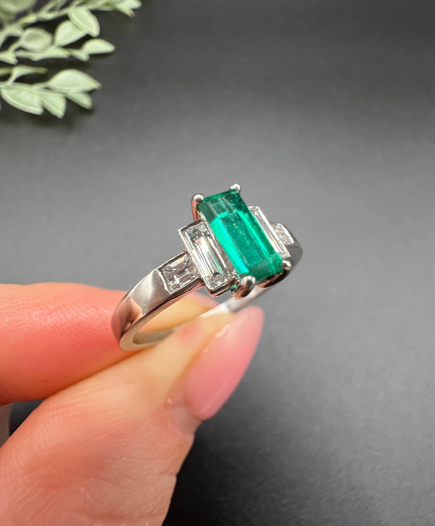 A five stone emerald cut emerald and baguette and square cut diamond ring in platinum, held in a hand