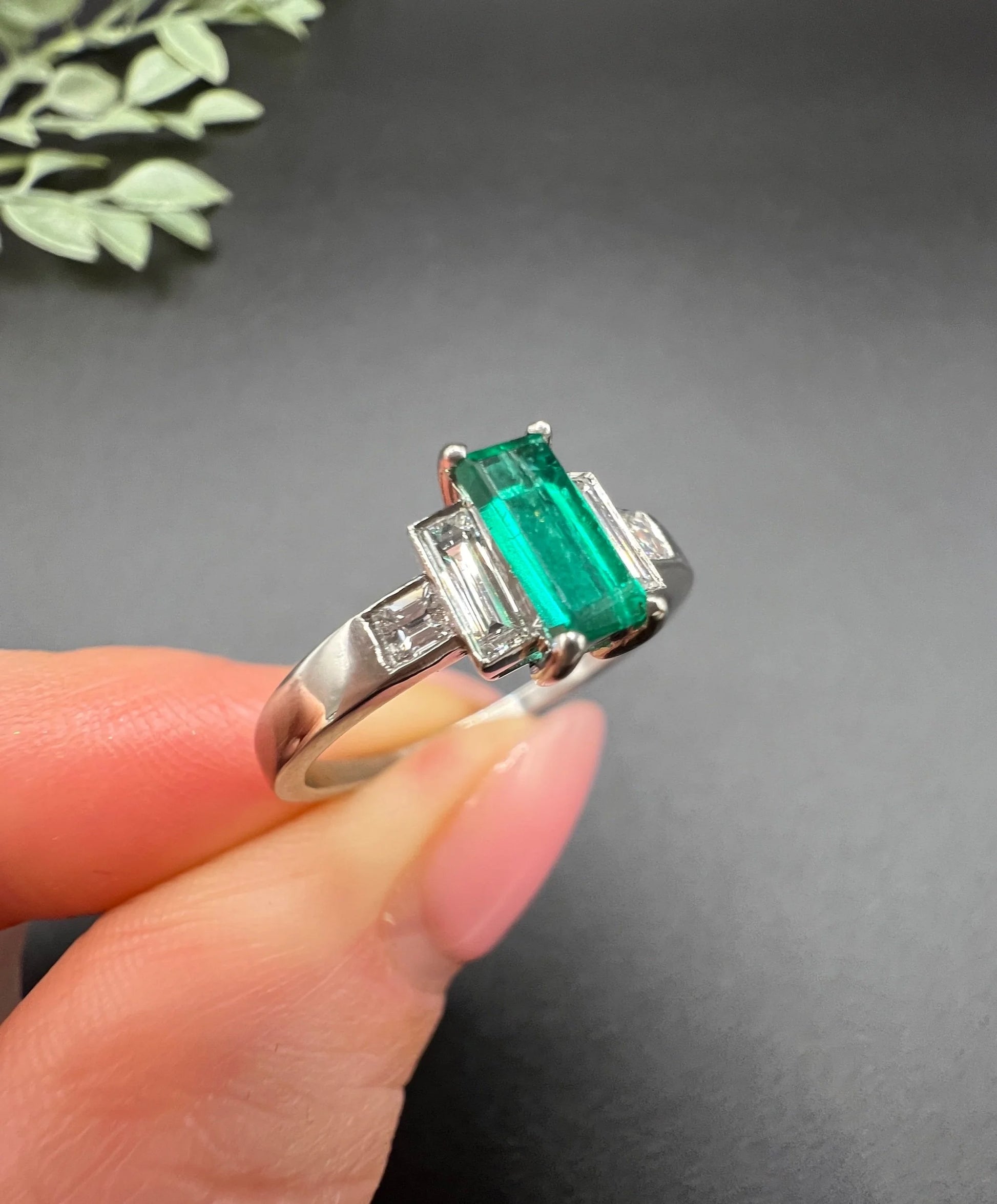 A five stone emerald cut emerald and baguette and square cut diamond ring in platinum, held in a hand