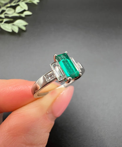 A five stone emerald cut emerald and baguette and square cut diamond ring in platinum, held in a hand