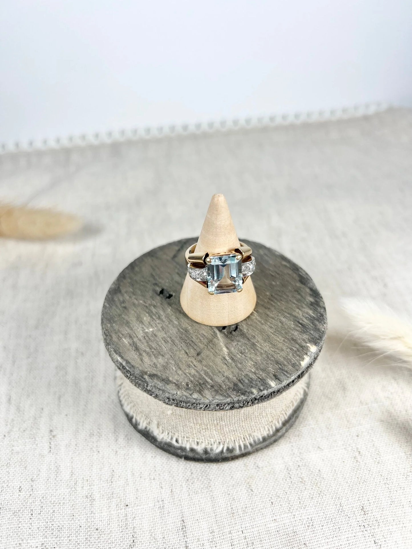 An aquamarine and diamond cocktail ring in gold, on a wooden ring cone
