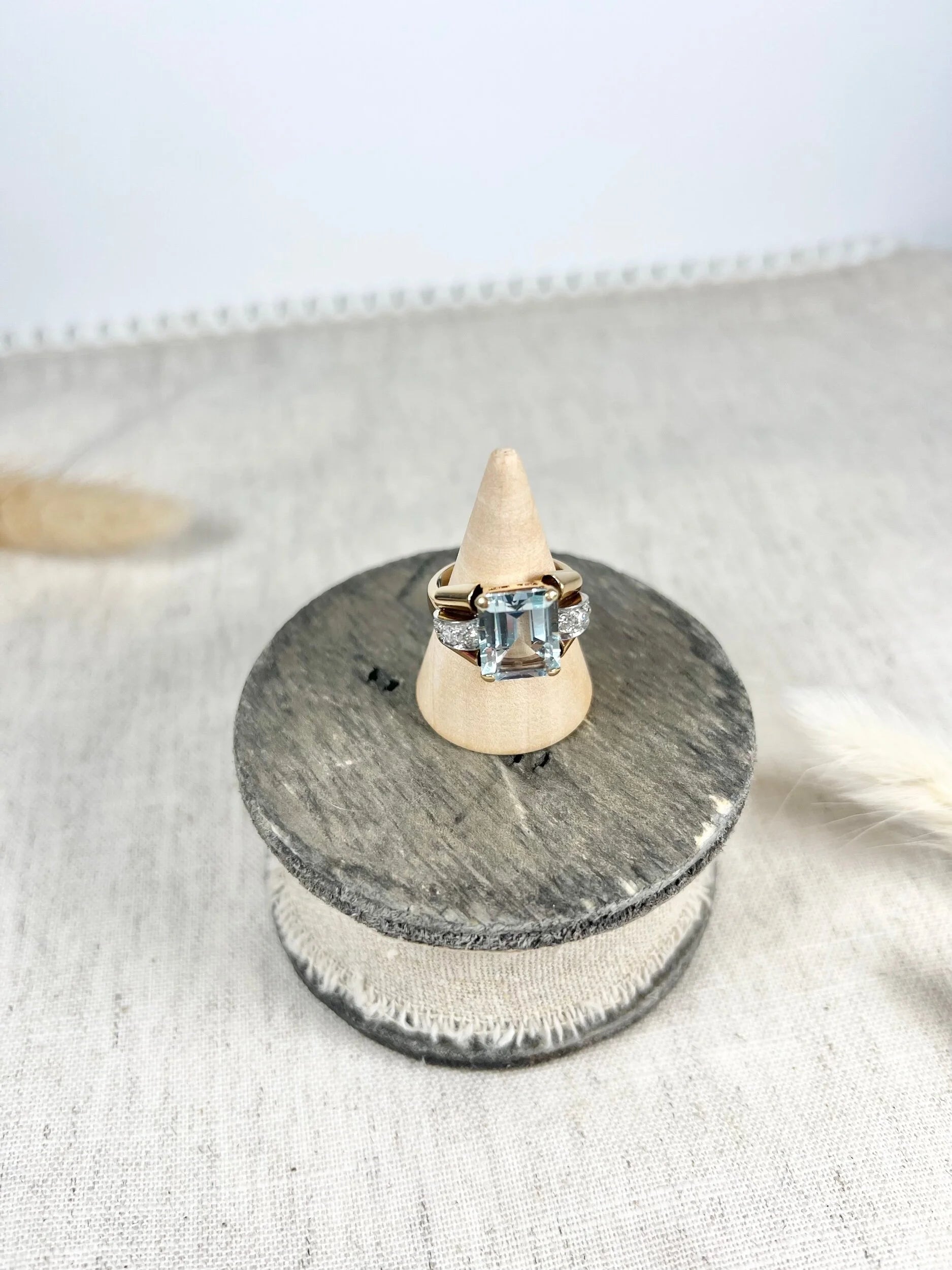 An aquamarine and diamond cocktail ring in gold, on a wooden ring cone