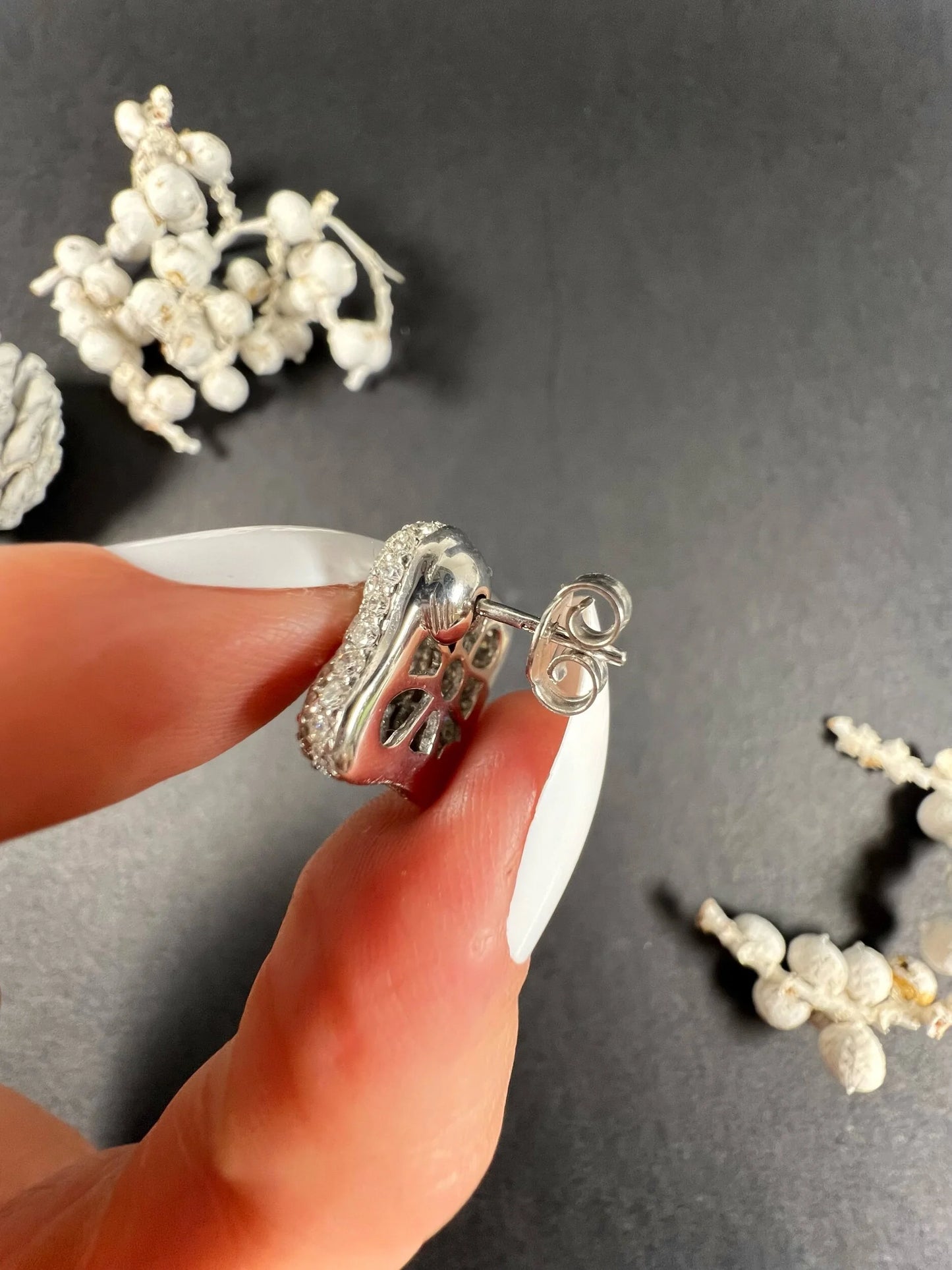 A white gold diamond earring, held in a hand