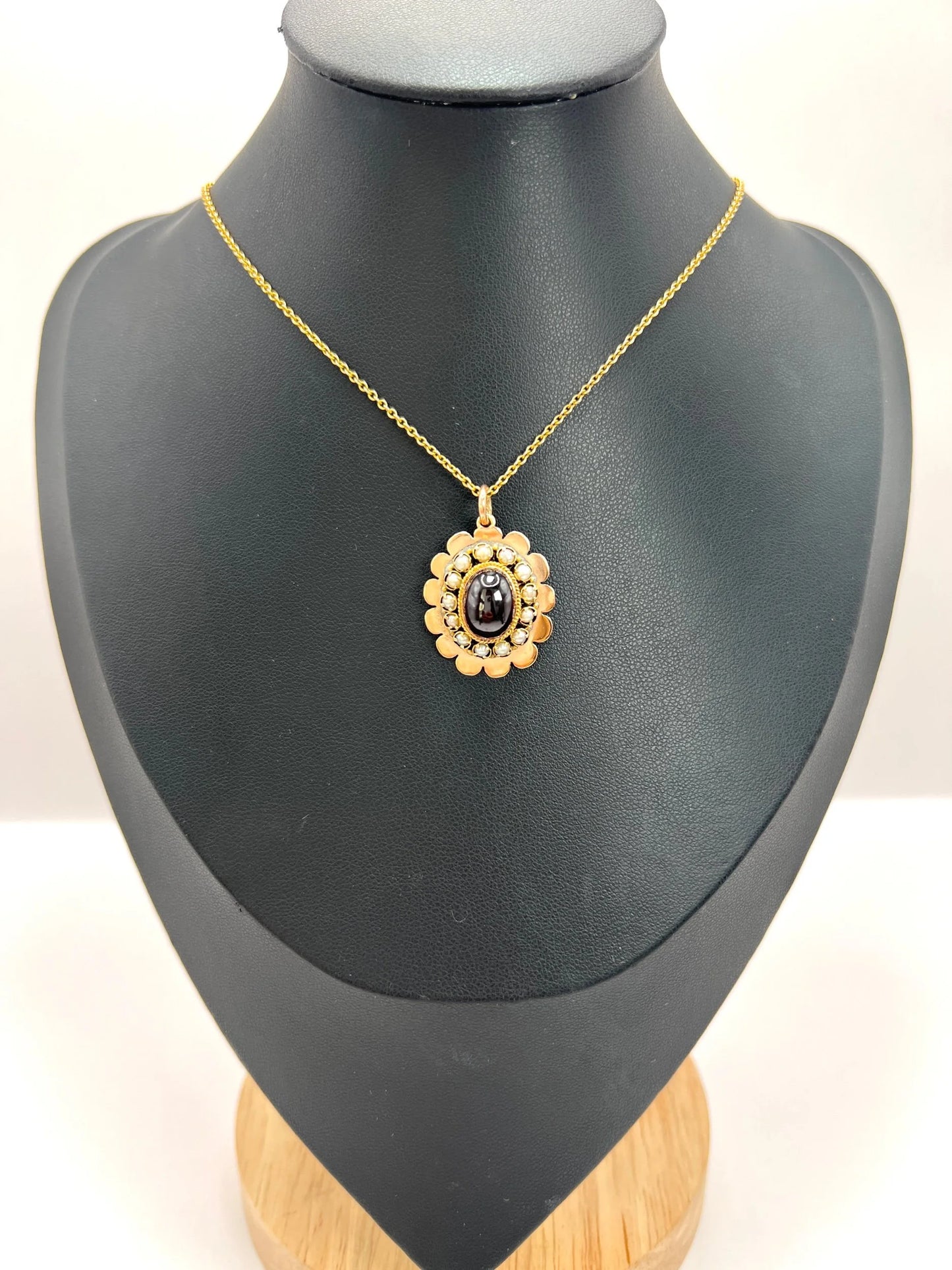A cabochon garnet pendant with a seed pearl border in rose gold, with a chain, on a black bust