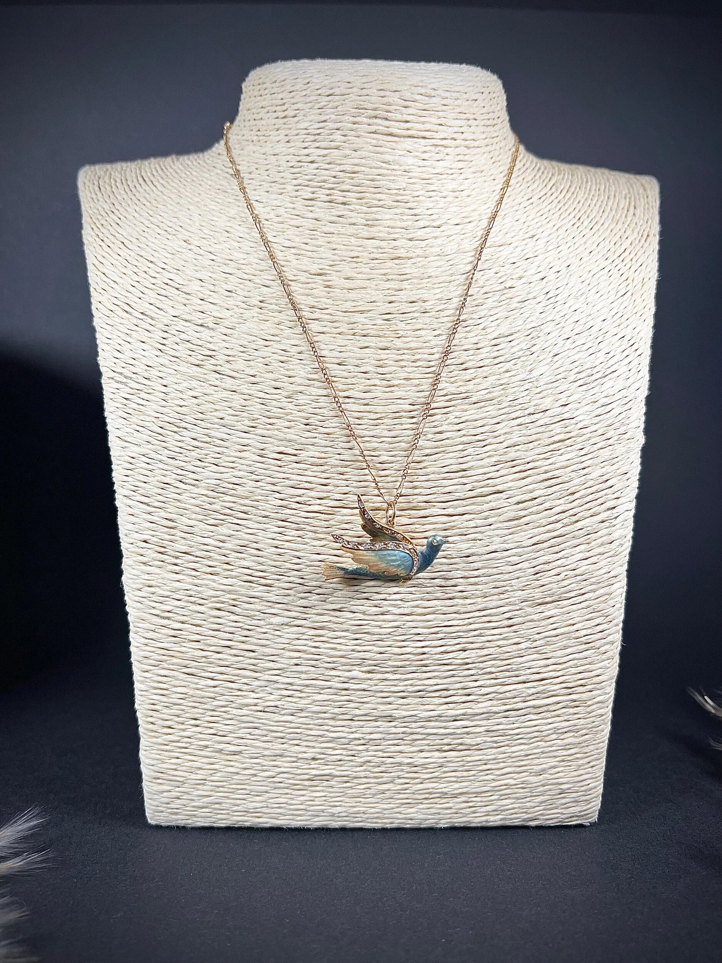 An enamel and diamond dove bird pendant, with a chain, on a jewellery display neck