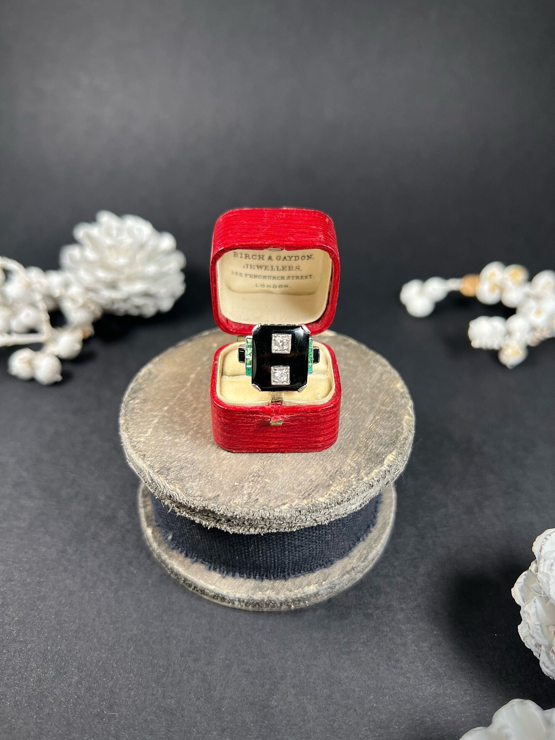 A geometric black onyx ring with diamonds and emeralds in white gold, in an antique ring box