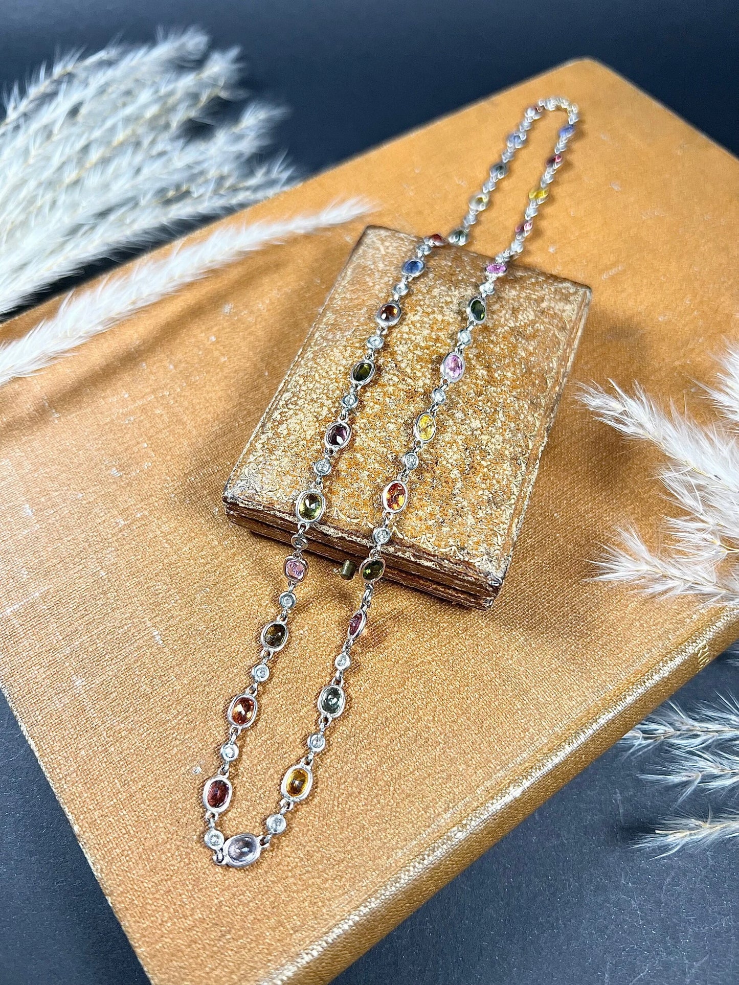 A coloured sapphire and diamond set necklace in platinum and gold, on an antique box and antique book