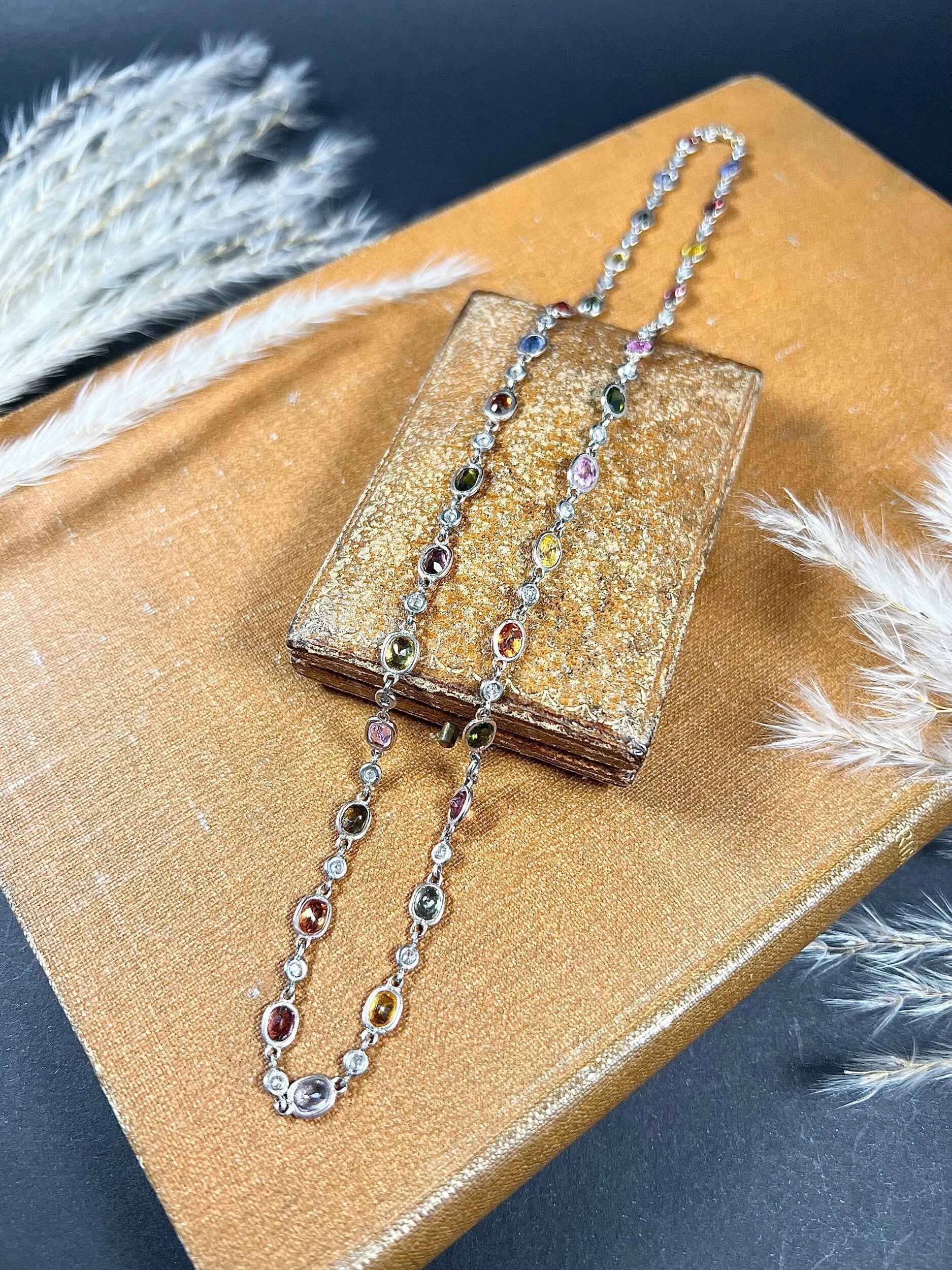 A coloured sapphire and diamond set necklace in platinum and gold, on an antique box and antique book