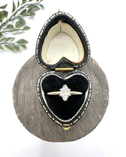 A marquise diamond solitaire ring in yellow and white gold, in a heart-shaped ring box