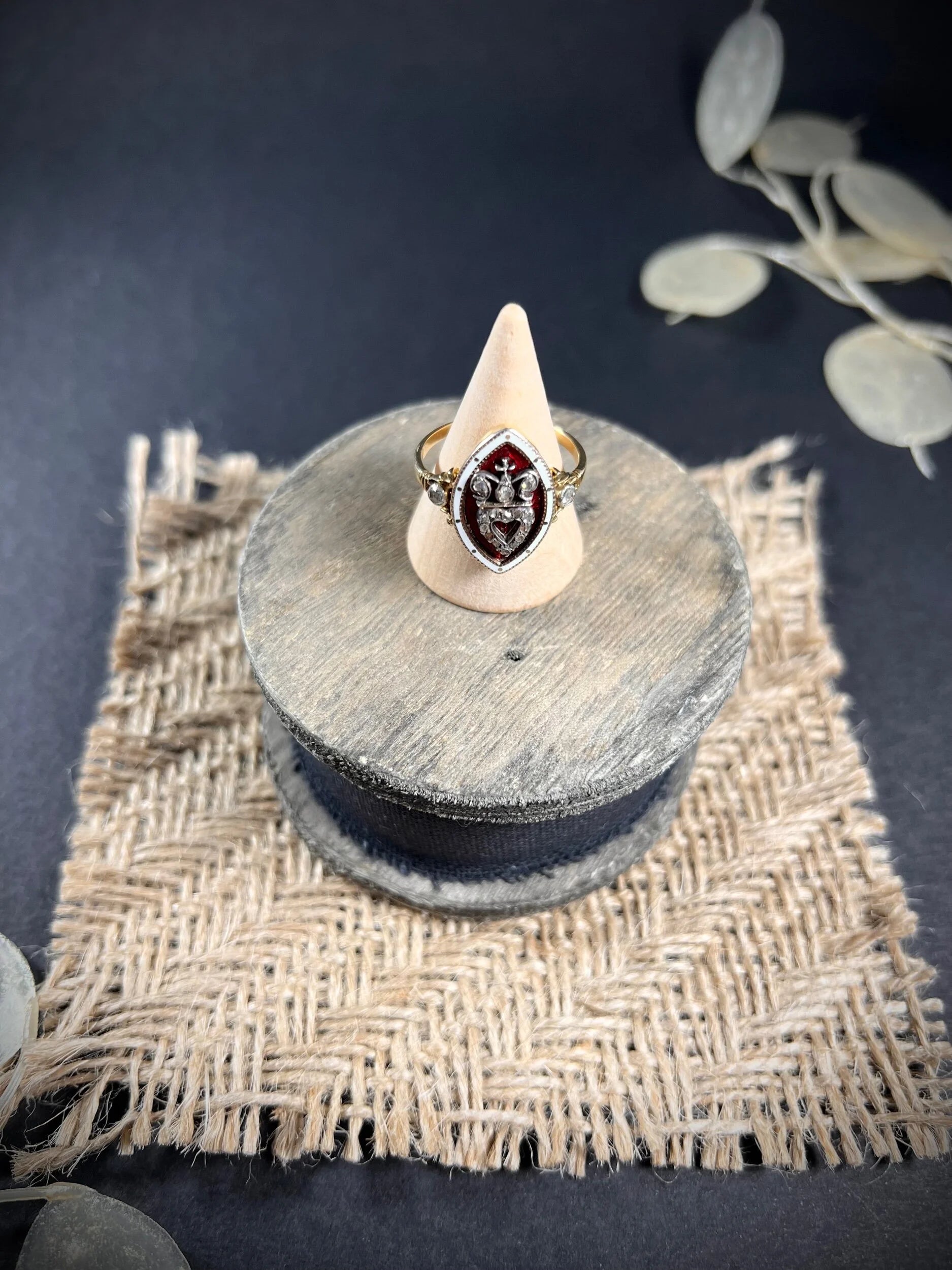 An ornate diamond and enamel navette shaped antique ring, on a ring cone, on top of a wooden spool