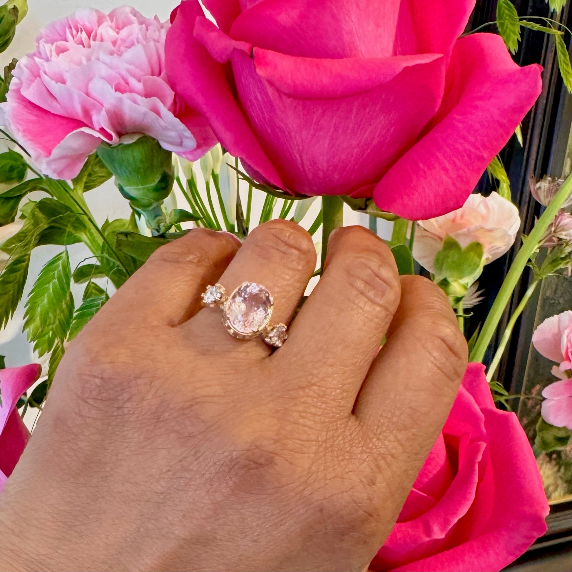 A three stone oval morganite and diamond ring in yellow gold, modelled on a hand