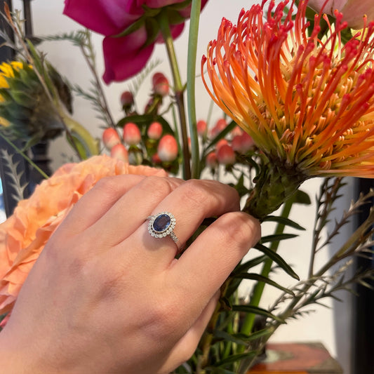 An oval sapphire and diamond cluster ring in platinum, modelled on a hand