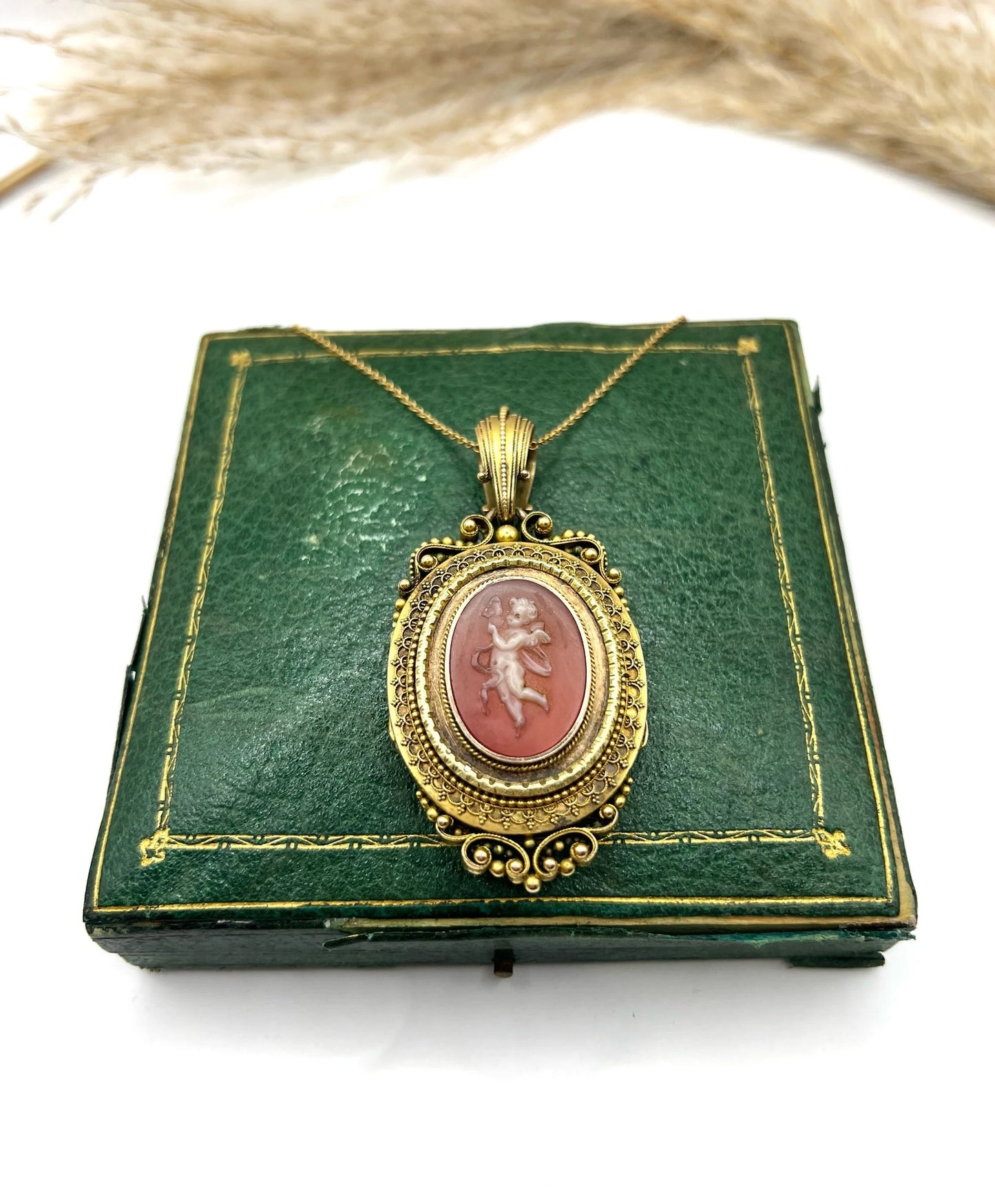 An ornate yellow gold oval cherub cameo locket pendant, with a gold chain, on an antique box