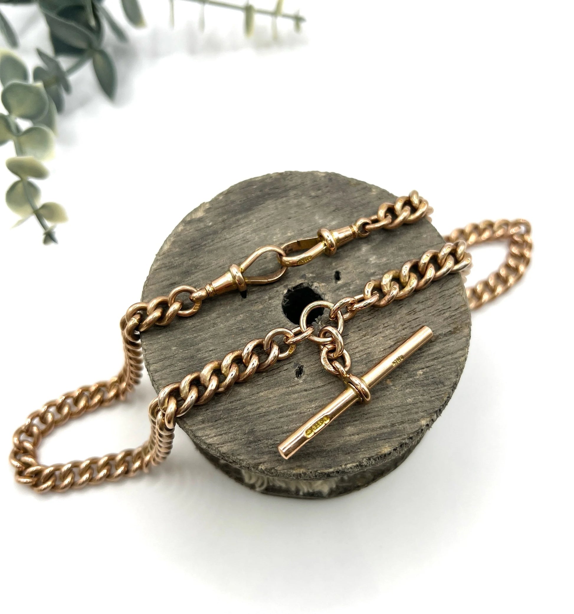 A rose gold curb link Albert chain on a white background
