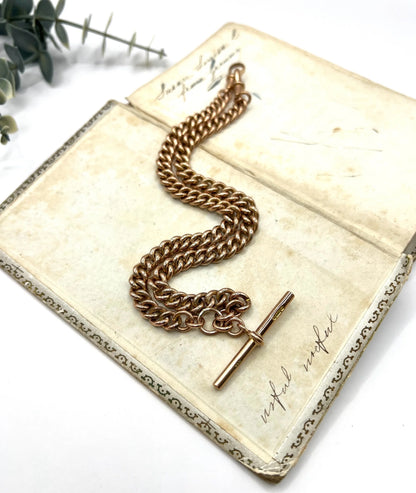 A rose gold curb link Albert chain lying on an antique book