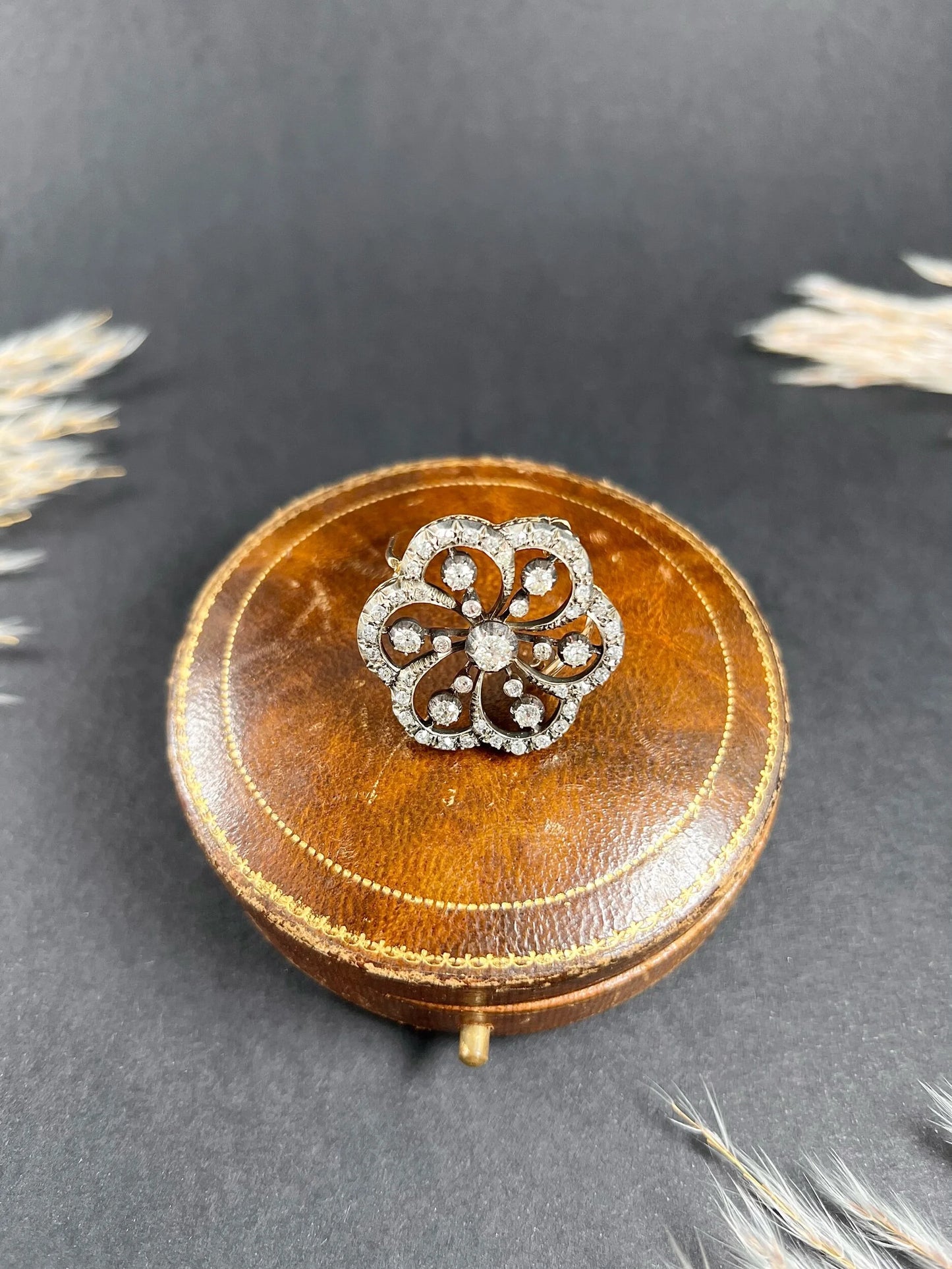 A floral design diamond set pendant/brooch on an antique brown jewellery box