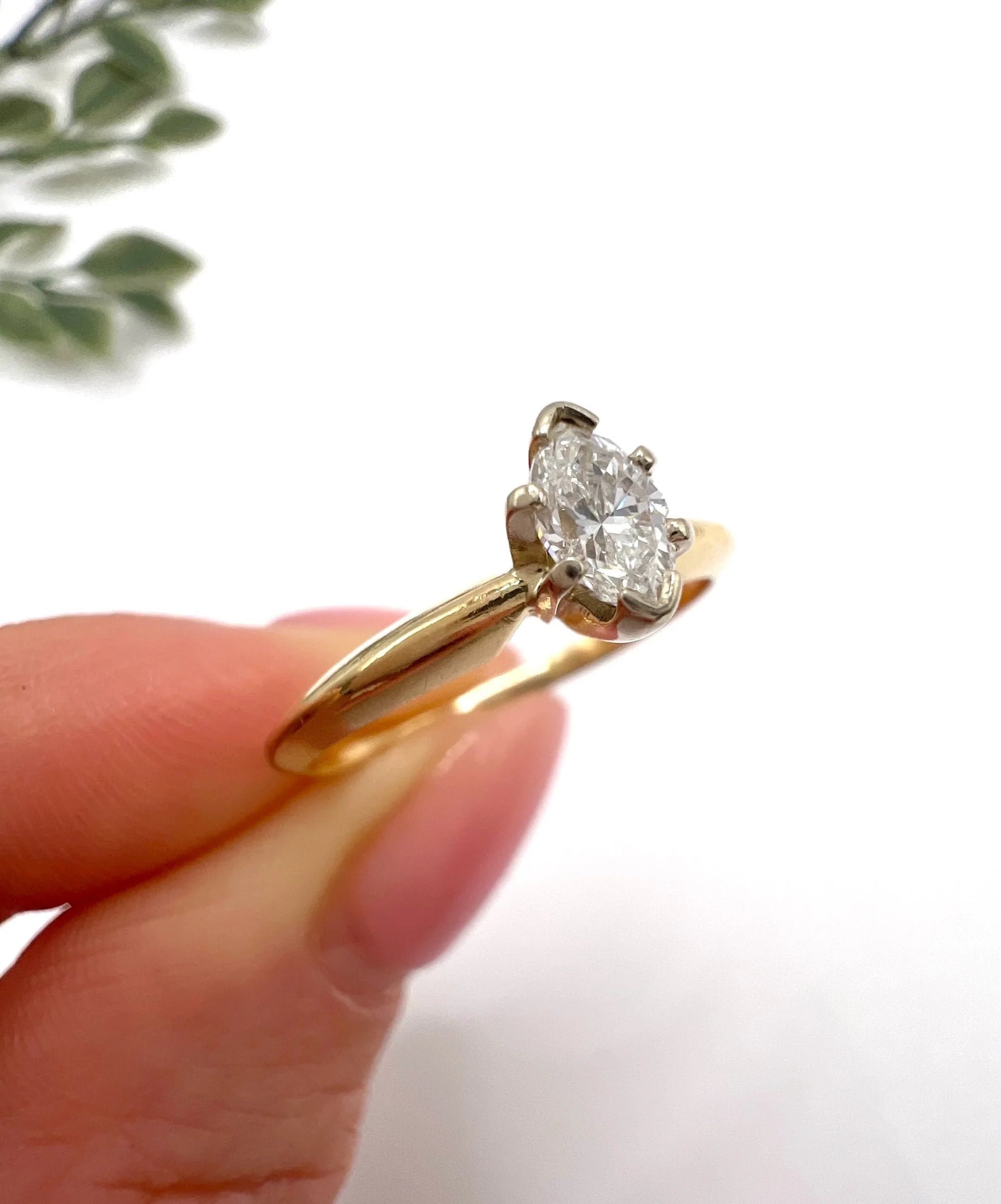 A marquise diamond solitaire ring in yellow and white gold, held in a hand