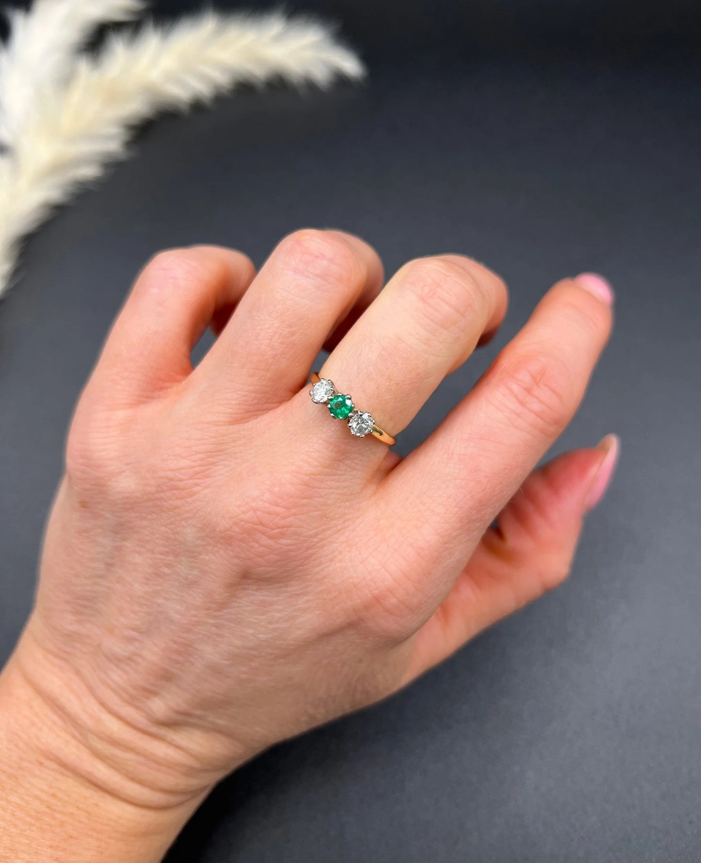A three stone emerald and diamond ring in yellow gold and platinum, modelled on a hand