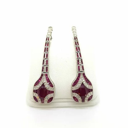 Art Deco Style Ruby, Diamond and Platinum Drop Earrings; featuring oval faceted rubies surrounded by calibre cut rubies and brilliant-cut diamonds set in a geometric design, suspended from an articulated graduated ruby and diamond set drop