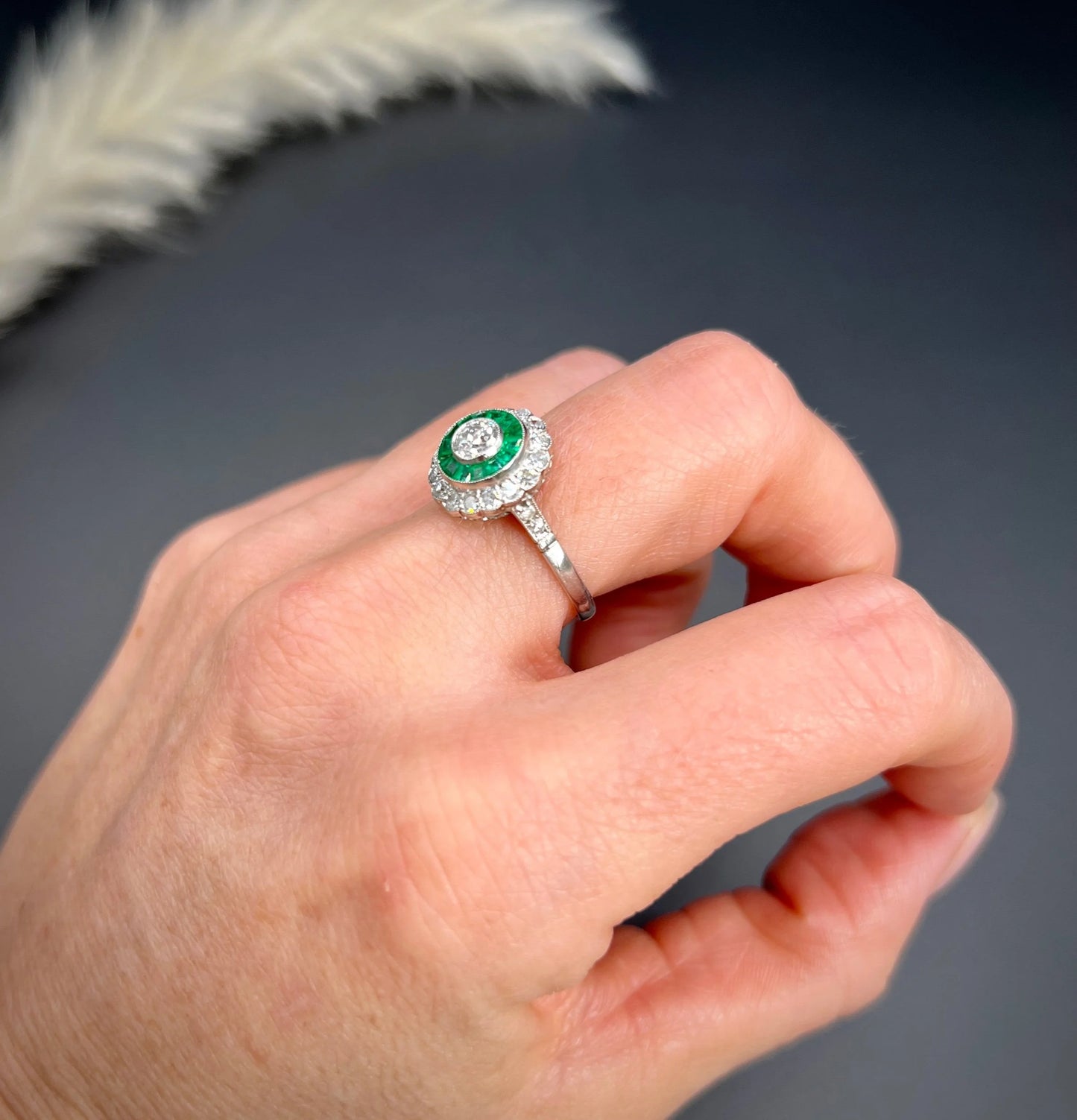 An emerald and diamond target cluster ring in platinum, modelled on a hand