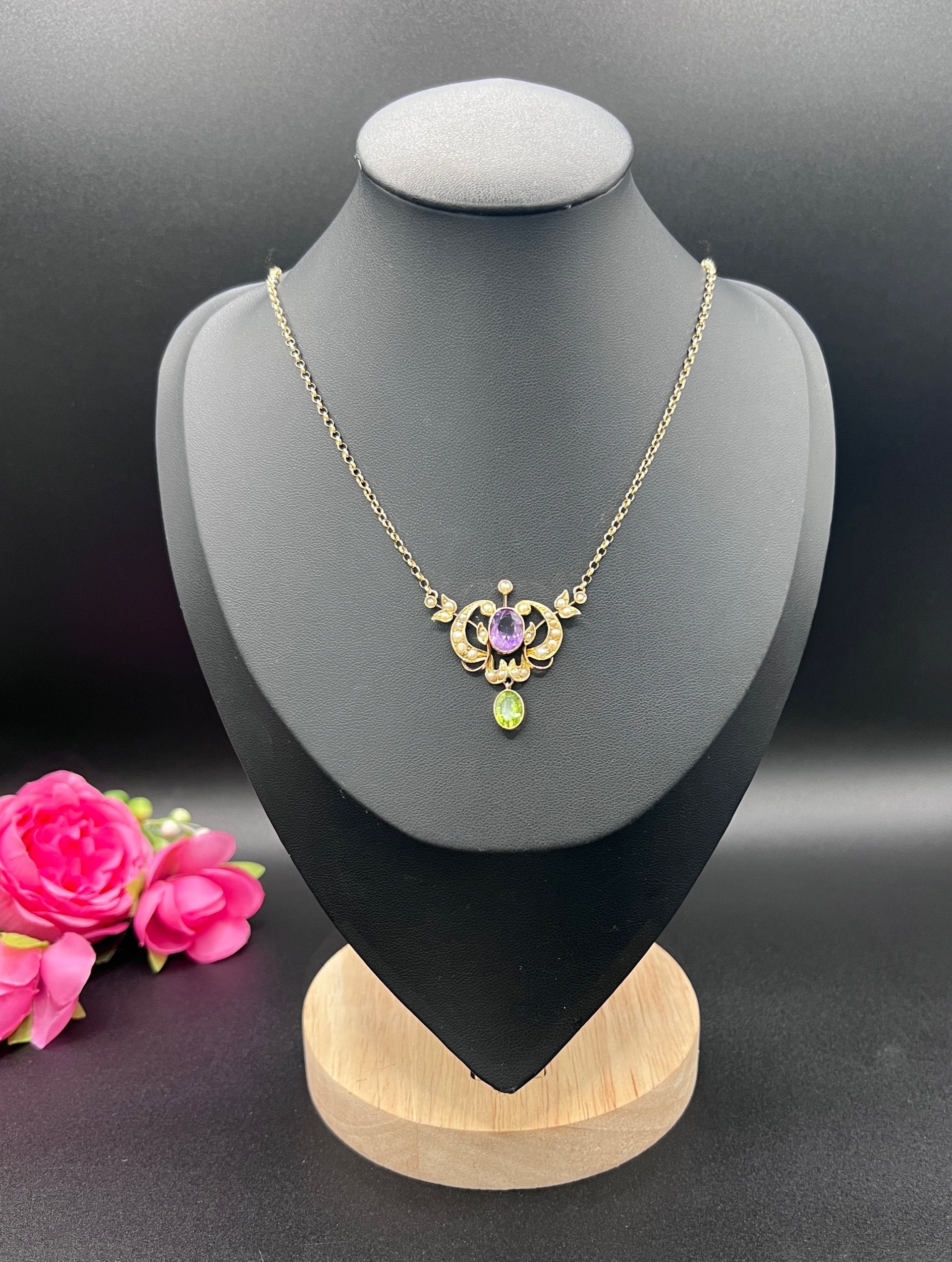 A yellow gold peridot, amethyst and seed pearl pendant necklace, on a black jewellery bust