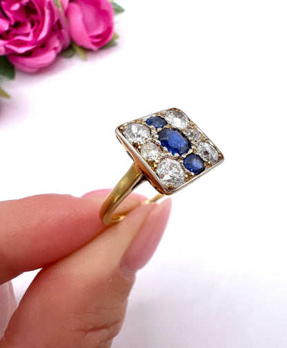 A square-shaped cluster ring with sapphires and diamonds in yellow gold and platinum, held in a hand