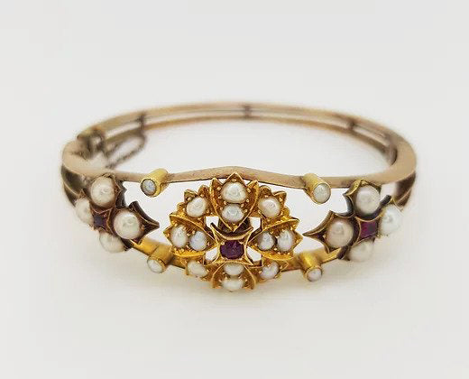 Antique Edwardian Pearl and Ruby Bangle; A delicate Edwardian bangle set with pearl clusters featuring central rubies. Marked for 15ct yellow gold.