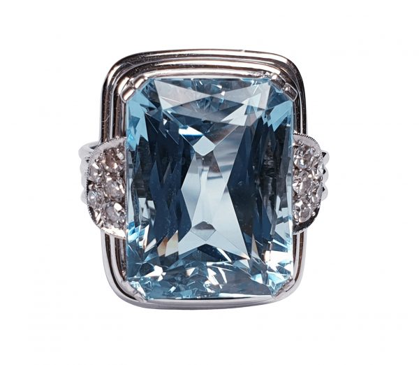 Art Deco Aquamarine and Diamond Dress Ring; a striking 14.80 carat emerald-cut aquamarine accented with half moon diamond cluster shoulders, on a three wire platinum band. Circa 1930s