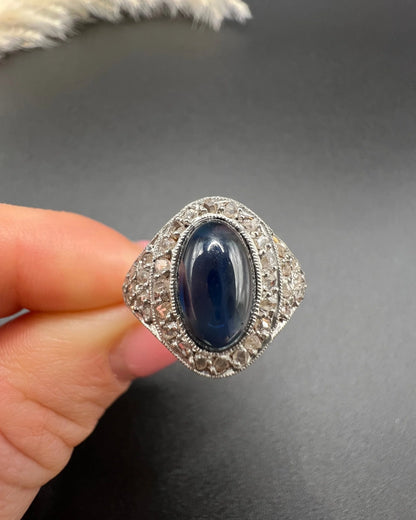 An oval cabochon sapphire and diamond fancy cluster ring in yellow and white gold, held in a hand