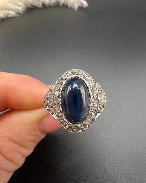 An oval cabochon sapphire and diamond fancy cluster ring in yellow and white gold, held in a hand