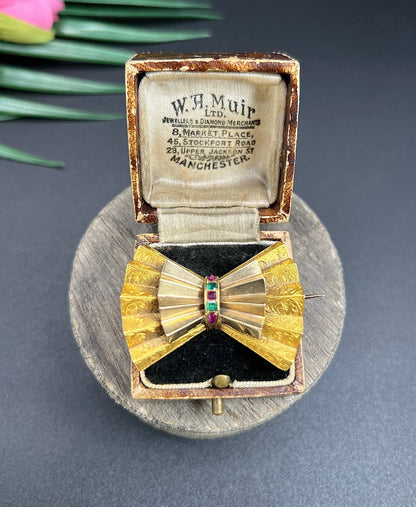 A yellow gold bow shaped brooch with rubies and emeralds