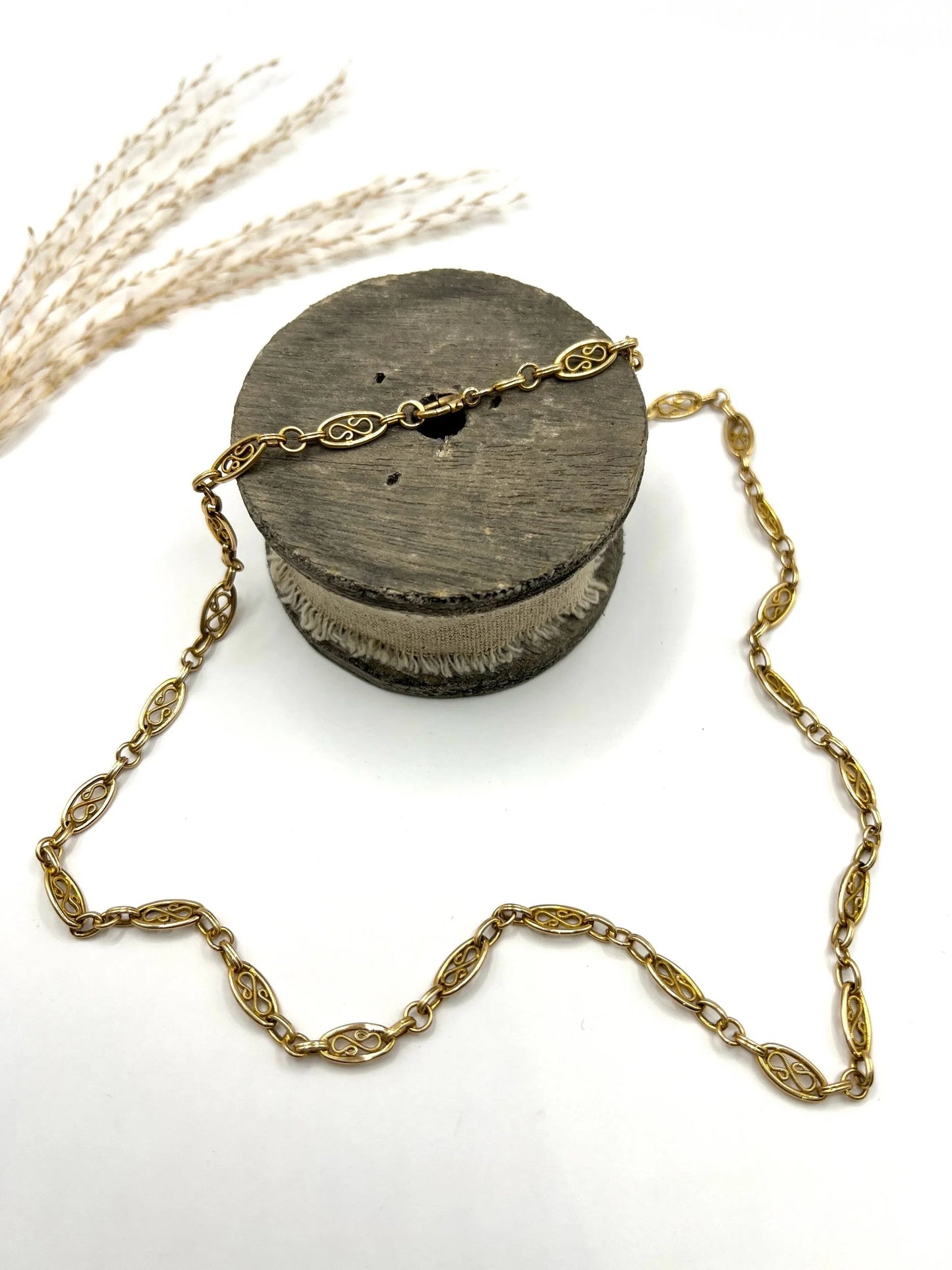 A yellow gold fancy link chain lying on a wooden object, on a white background